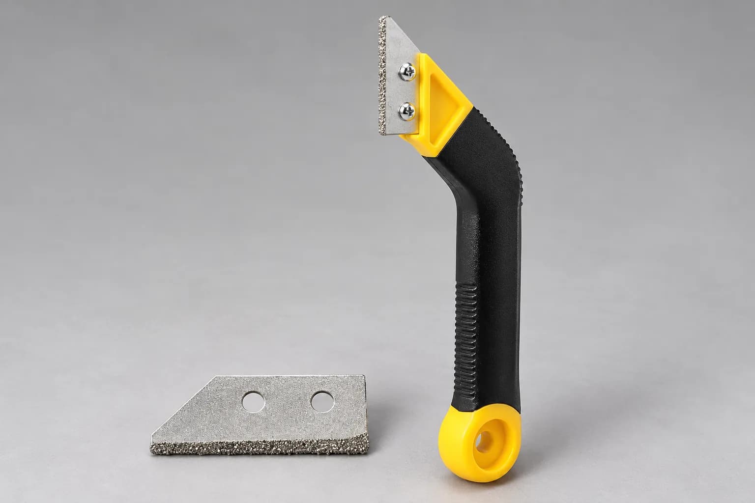 Grout remover with black and yellow handle beside a spare carbide blade